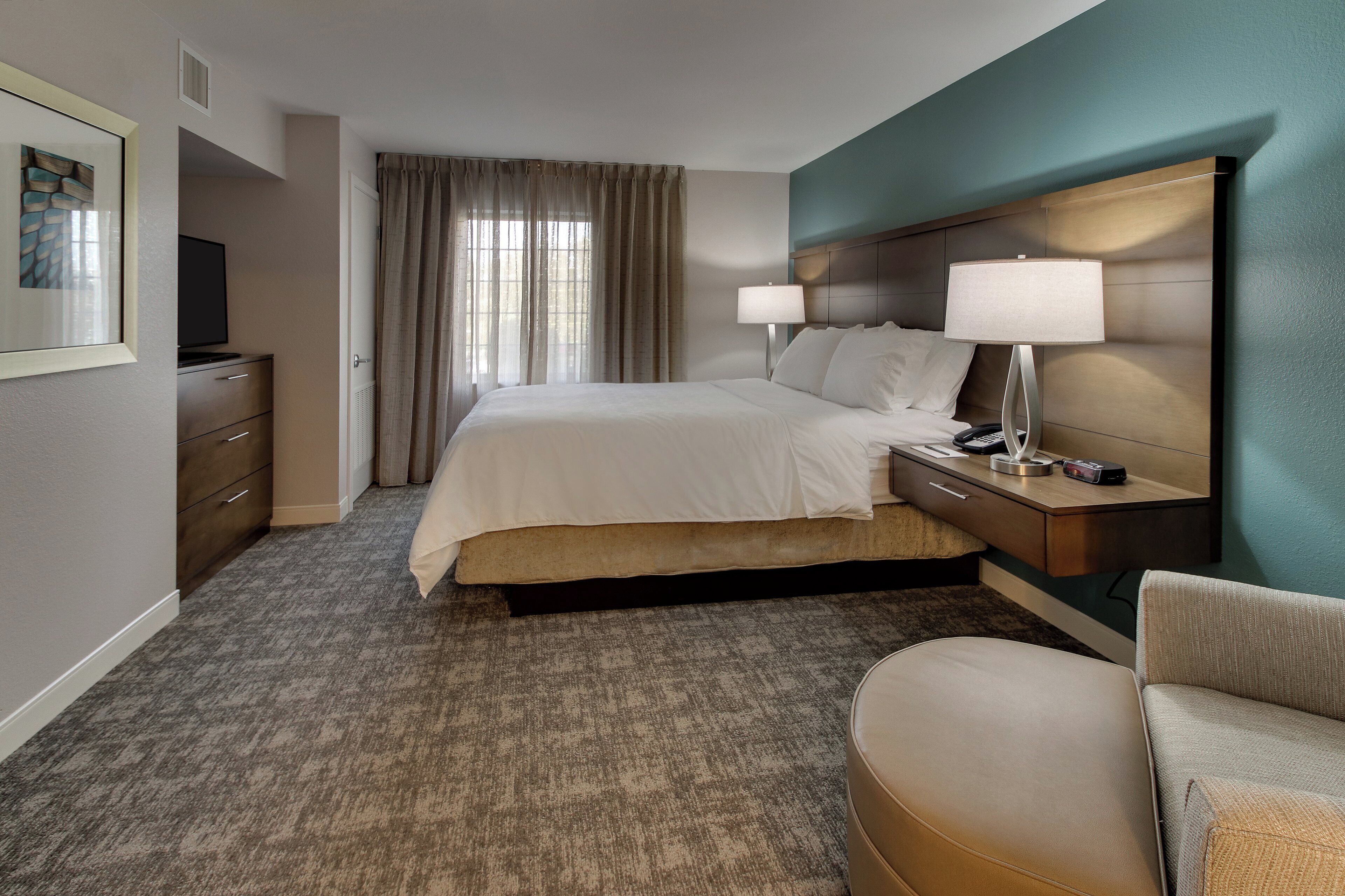 Una habitación de hotel con una cama, mesita de noche, lámpara y una silla.