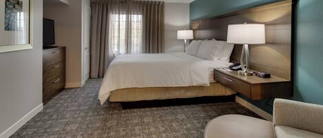 Una habitación de hotel con una cama, mesita de noche, lámpara y una silla.