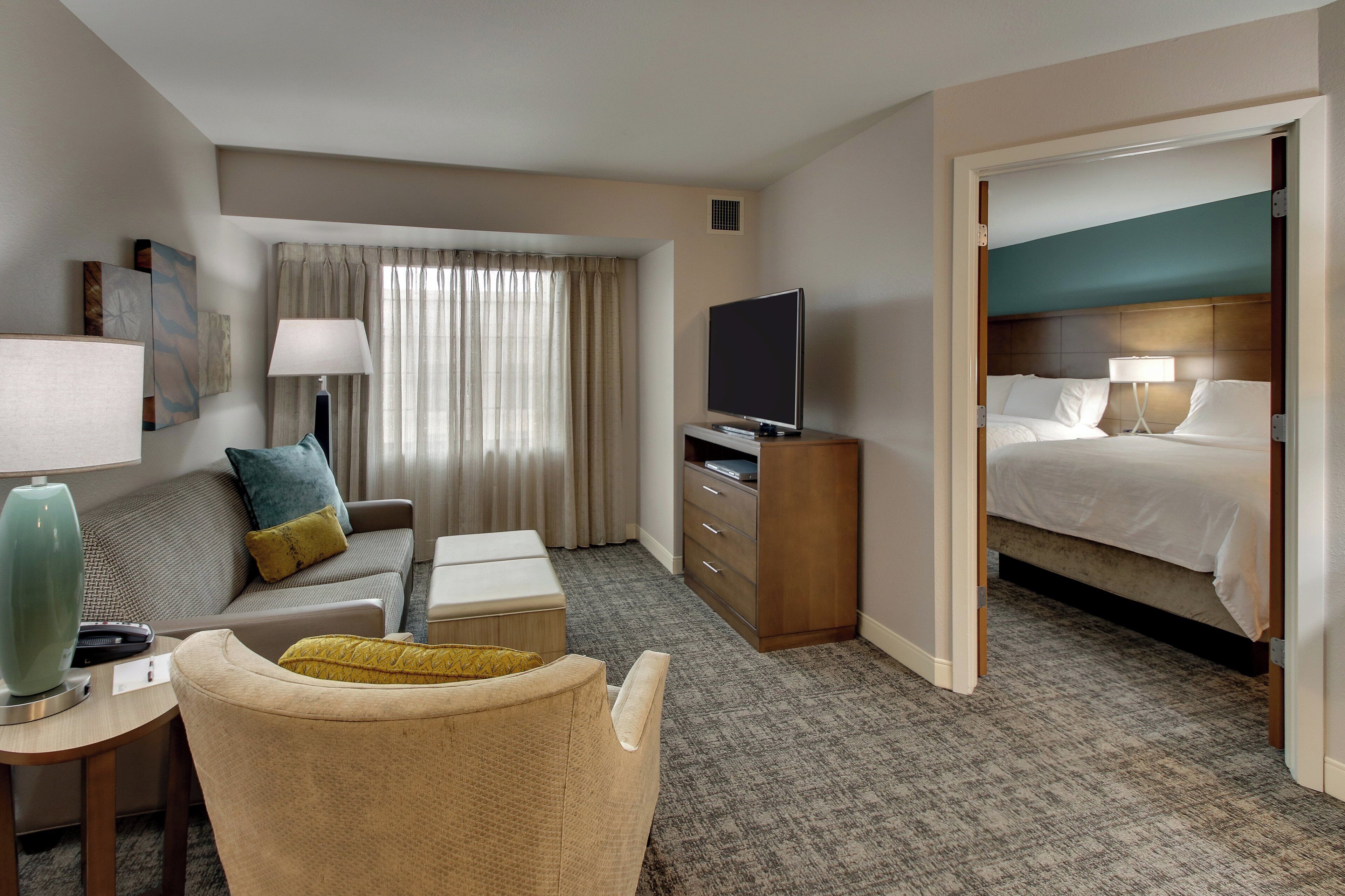 Una habitación de hotel con cama, televisión, escritorio con lámpara, silla y sofá.