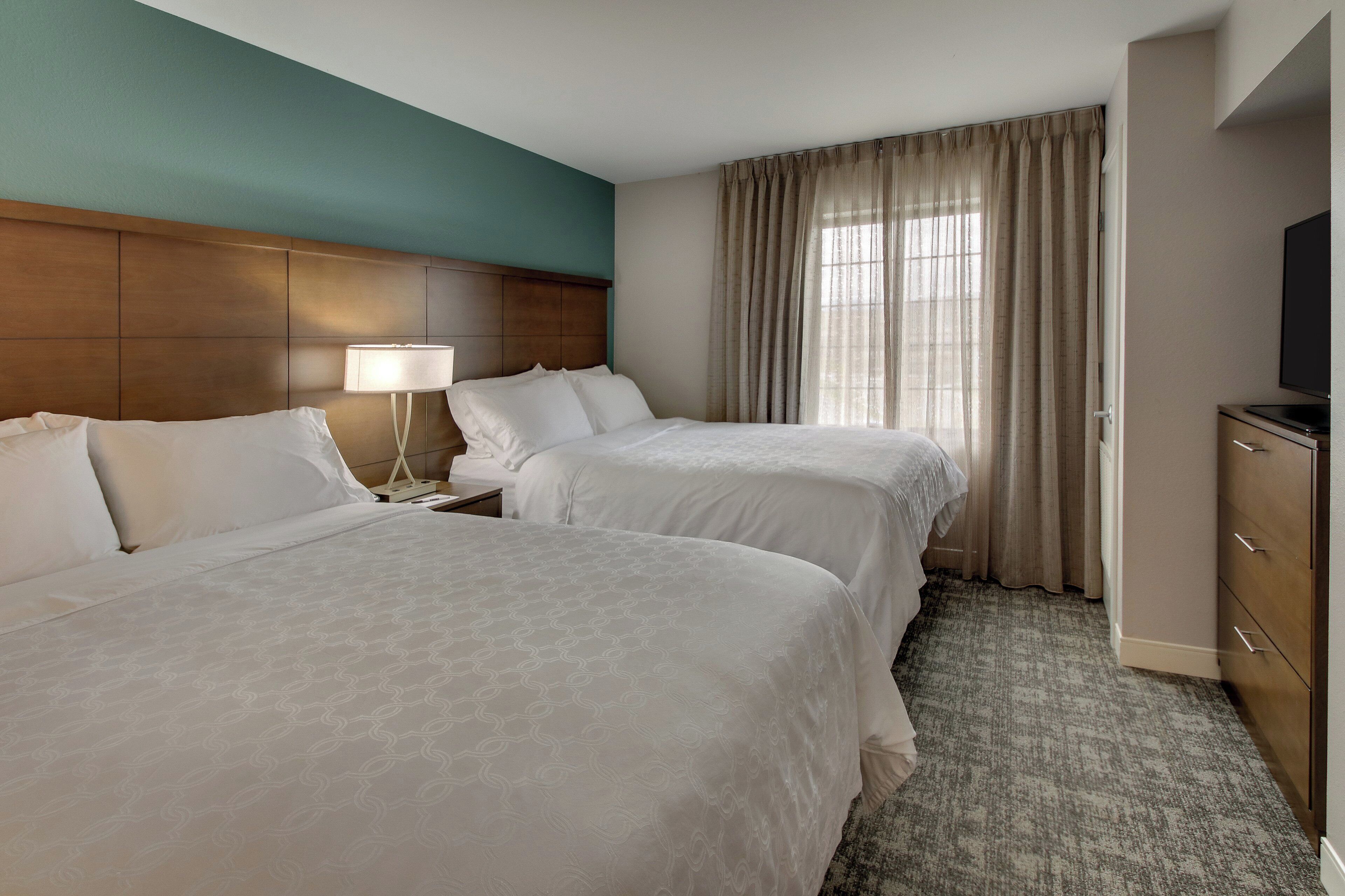 A hotel room with two beds, a nightstand with a lamp, a TV, and a wardrobe.