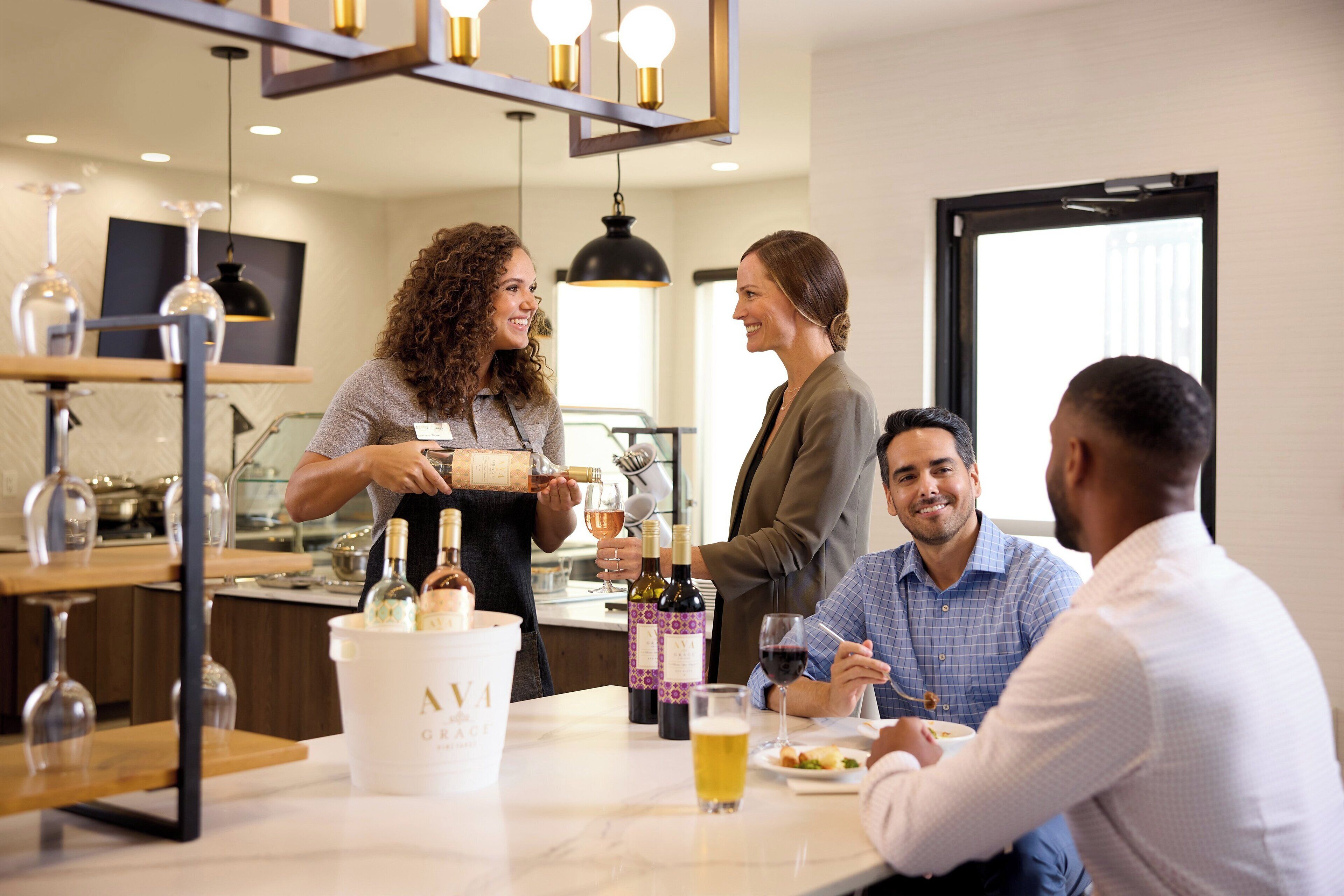 A group of people in a modern dining area with a bar, wine bottles, and glasses on the table.