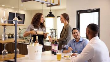 A group of people in a modern dining area with a bar, wine bottles, and glasses on the table.