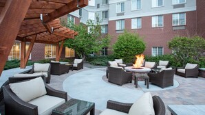 An outdoor patio with wicker furniture, a fire pit, and a brick building in the background. - Staybridge Suites Denver International Airport by IHG (Denver)