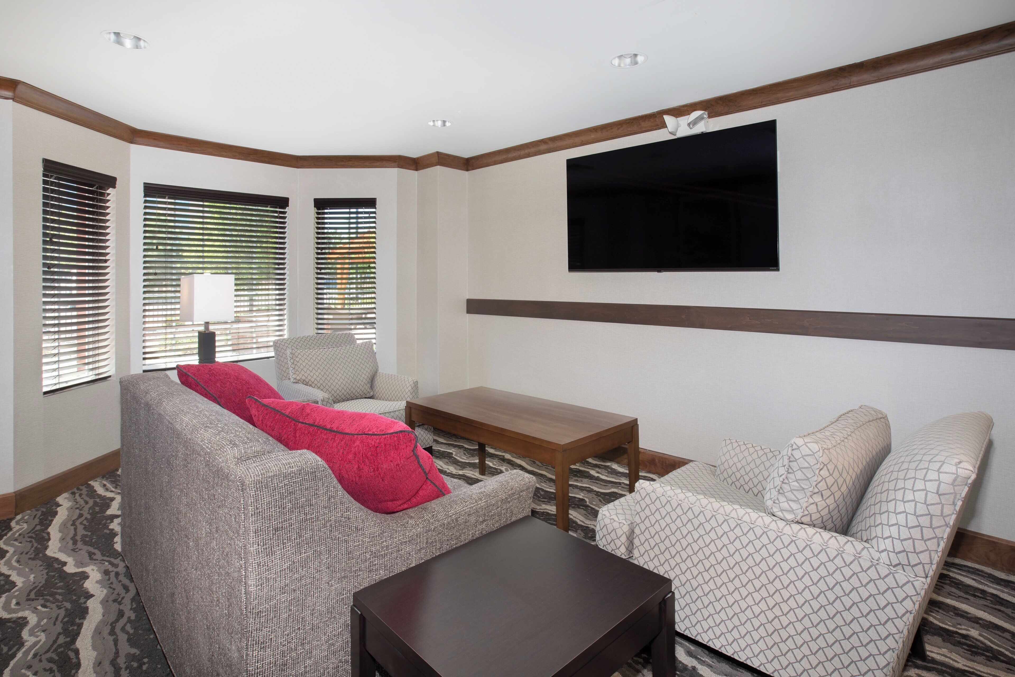 A hotel room with a sofa, armchair, a small wooden table, and a flat-screen TV mounted on the wall.