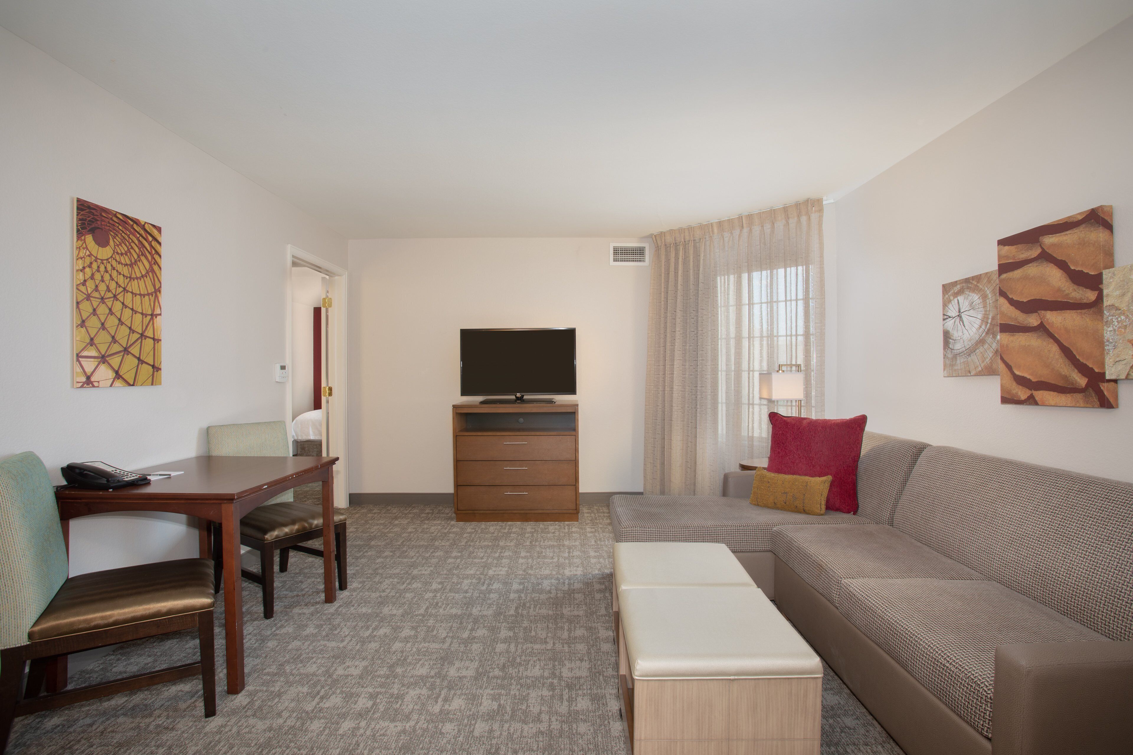 A hotel room with a wooden desk, two chairs, a television, a sofa, and artwork on the walls.