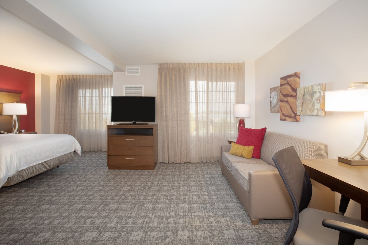 A hotel room with a bed, a desk, a chair, a television, and a sofa.