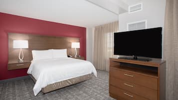 A hotel room with a bed, two bedside lamps, a TV on a wooden stand, and a carpeted floor.