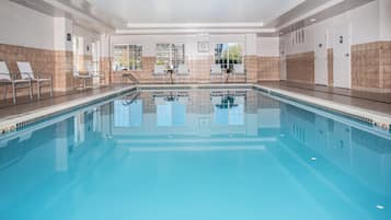 An indoor swimming pool with clear water, surrounded by walls with a tiled pattern, and equipped with lounge chairs and a small table.