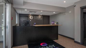 Mostrador de recepción del hotel COAST Innisfail con dispensador de agua, una planta pequeña y un cartel sobre el mostrador.