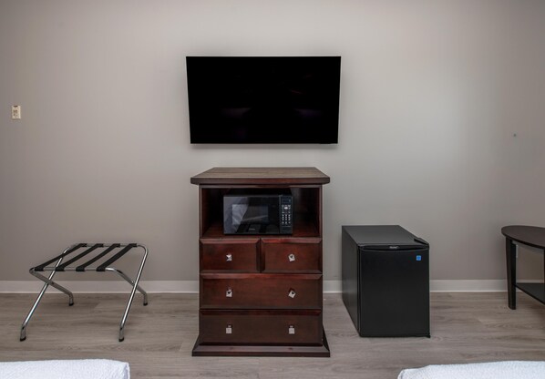 A room with a flat-screen TV mounted on the wall, a wooden chest of drawers with a microwave on top, a compact refrigerator, and a metal drying rack. - Coast Innisfail Hotel  (Innisfail)