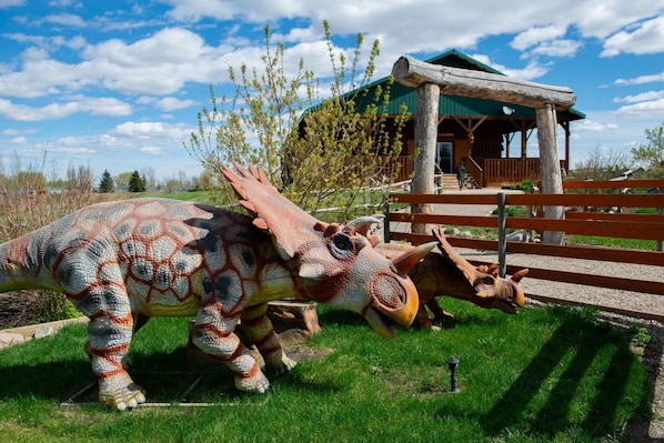 A dinosaur statue in a grassy area with a wooden structure in the background.