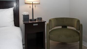 Ein ordentlich bezogenes Bett mit weißer Decke, ein Nachttisch mit Lampe, Taschentuchbox und digitaler Uhr.