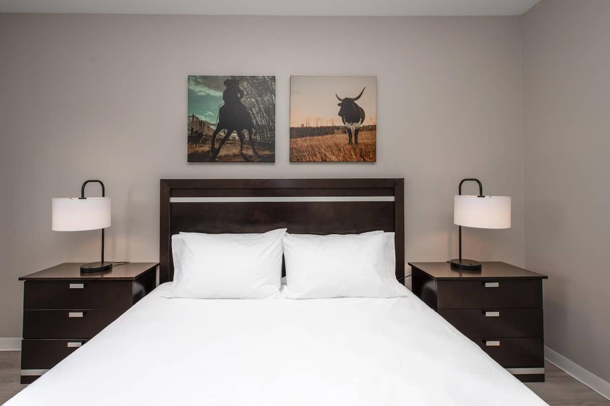 Une chambre d’hôtel avec un grand lit, deux tables de chevet, deux lampes fixées au mur et deux tableaux encadrés.