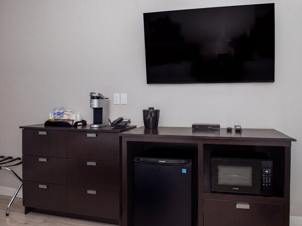 A hotel room with a dark wooden desk, a coffee machine, a phone, a remote control, a microwave, and a flat-screen TV mounted on the wall. - Coast Innisfail Hotel  (Innisfail)