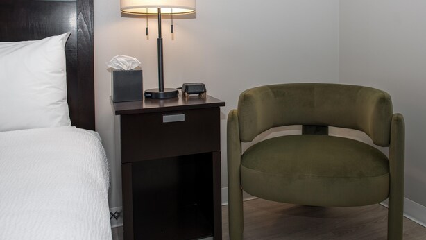 A neatly made bed with a white comforter, a bedside table with a lamp, a tissue box, and a digital clock.