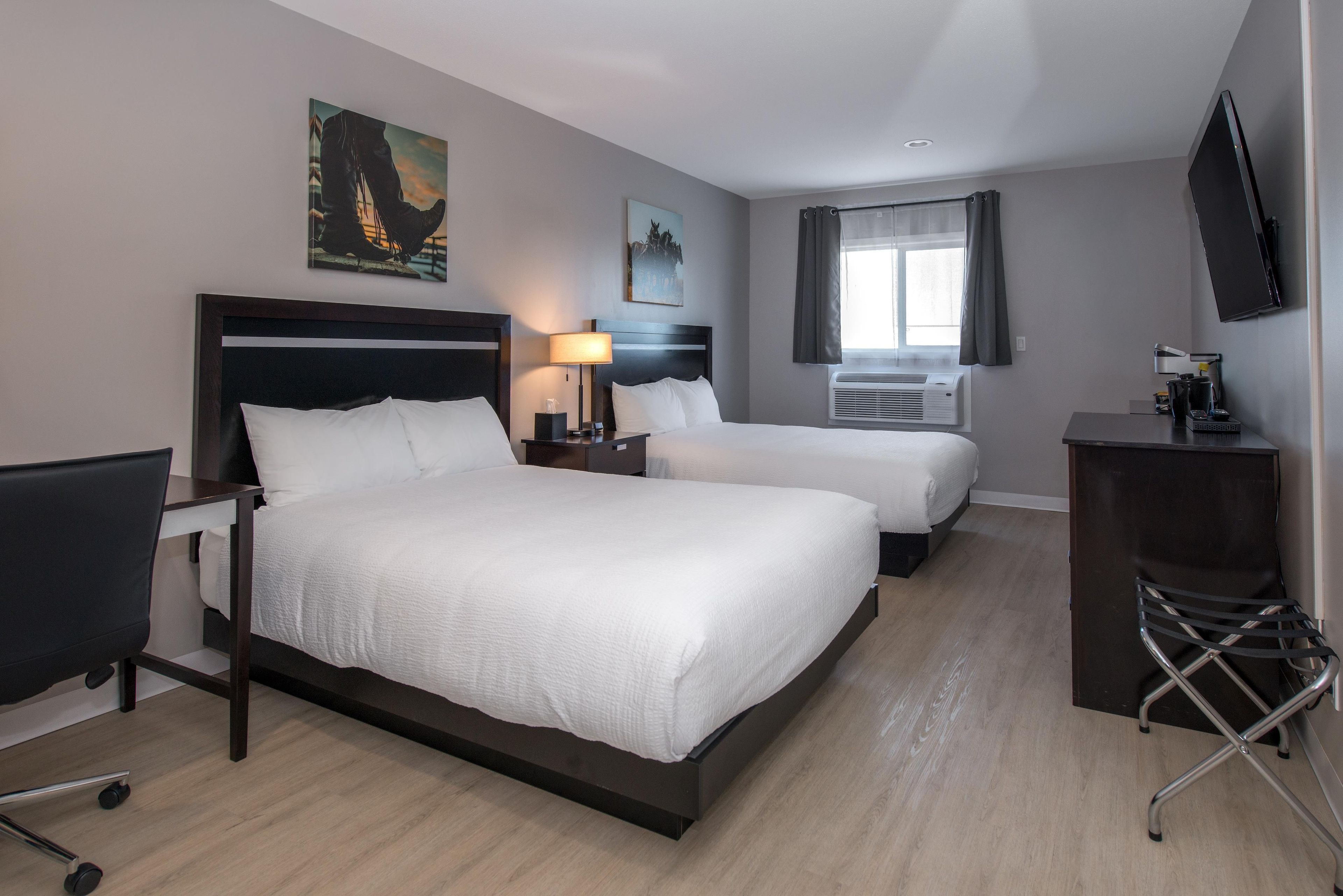 Una habitación de hotel con dos camas, un escritorio, una silla, un televisor y obras de arte en las paredes.