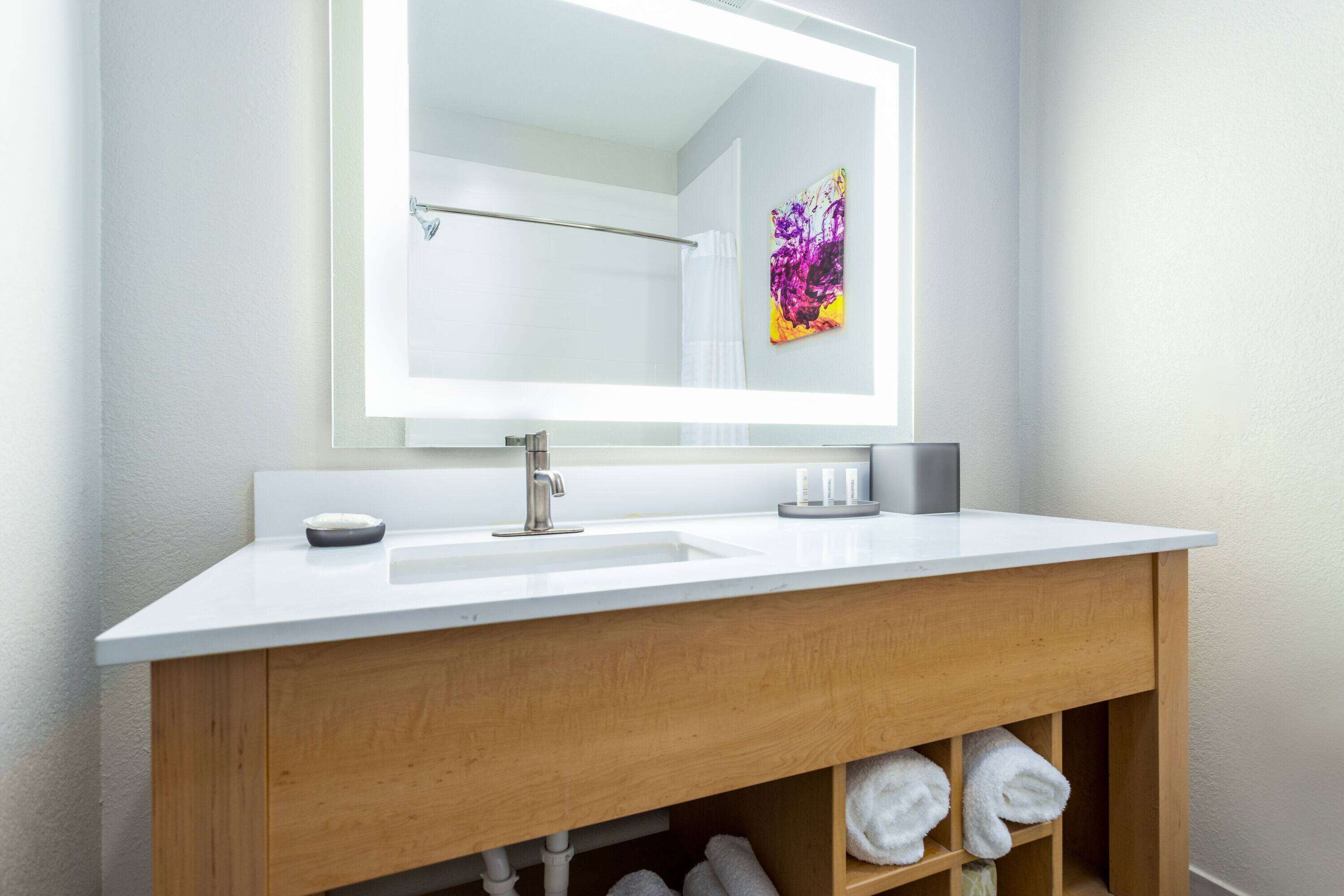 Ein modernes Badezimmer mit einem weißen Waschbecken, einer Holz-Kommode und einem großen Spiegel.