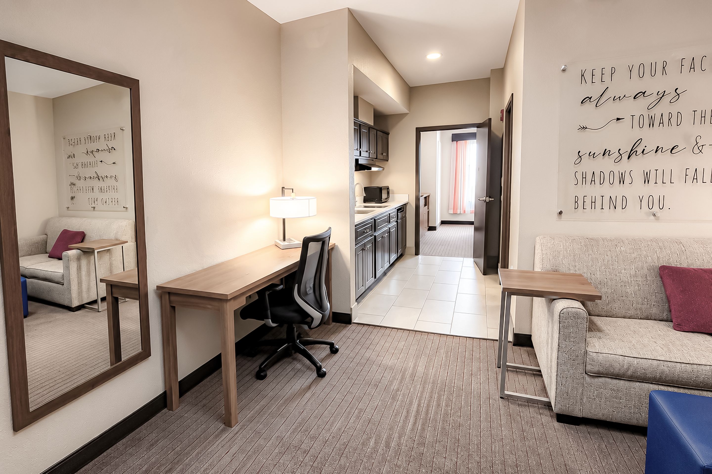 Une chambre d’hôtel équipée d’un bureau, d’une chaise et d’un canapé. Un miroir est accroché au mur, ainsi qu’une citation inspirante.