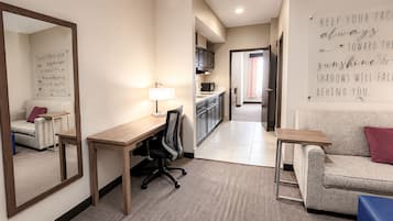 Une chambre d’hôtel équipée d’un bureau, d’une chaise et d’un canapé. Un miroir est accroché au mur, ainsi qu’une citation inspirante.