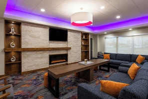 A modern living room with a fireplace, a flat-screen TV, and a sofa with orange cushions. - La Quinta Inn & Suites by Wyndham Augusta/Fort Eisenhower (Augusta)