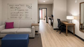Habitación de hotel con sofá, reposapiés, escritorio, silla y una cita motivacional en la pared.