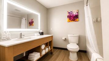 A modern bathroom with a large mirror, a sink, a toilet, and a shower.