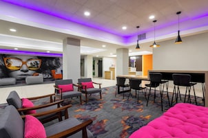 Un moderno vestíbulo de hotel con zona de bar, arreglos de asientos y una alfombra colorida.