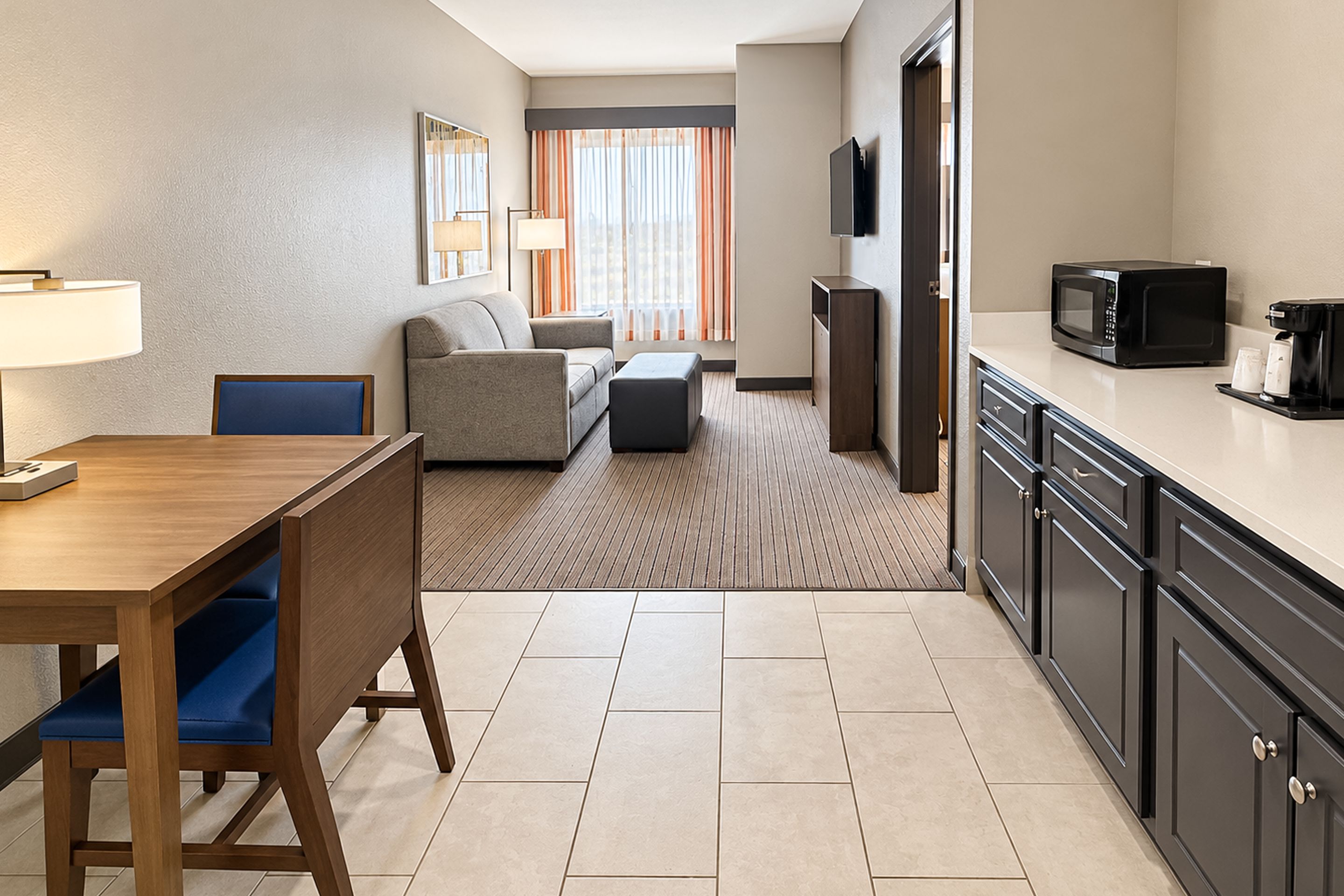 A hotel room with a dining table, a sofa, a TV, and a kitchenette.