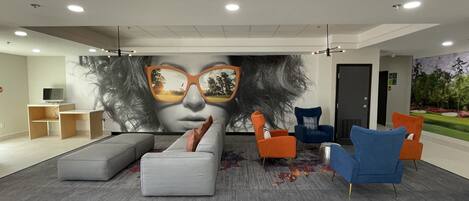 A modern lobby with a large mural, comfortable seating, and a flat-screen TV.