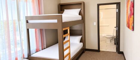 A bunk bed room with a window, curtains, an air conditioning unit, and a bathroom visible through an open door.