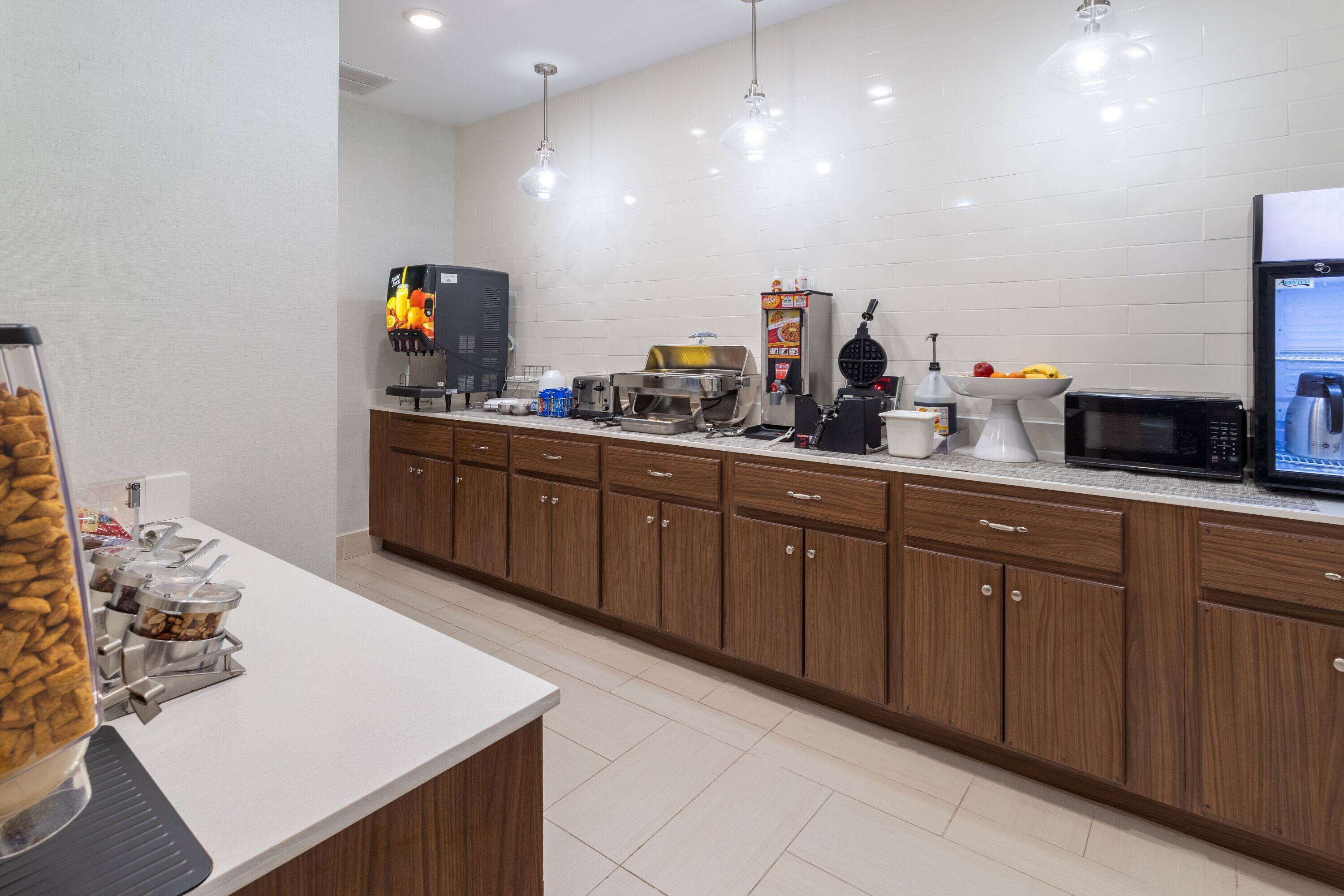 A modern kitchen with wooden cabinets, a microwave, a coffee machine, and a food display.