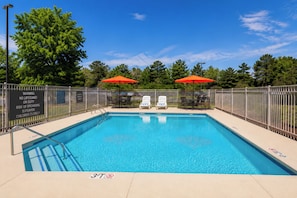 A rectangular swimming pool with a metal fence, two red umbrellas, and a warning sign. - La Quinta Inn & Suites by Wyndham Augusta/Fort Eisenhower (Augusta)