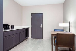 A compact kitchen with a microwave, coffee maker, and a cabinet. There's a door and a table with a chair. - La Quinta Inn & Suites by Wyndham Augusta/Fort Eisenhower (Augusta)