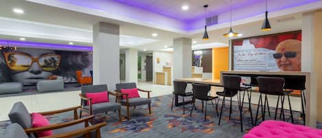 A modern hotel lobby with seating areas, a reception desk, and a mural on the wall.