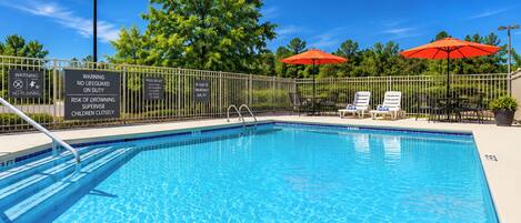 A swimming pool with a fenced area, warning signs, and umbrellas.