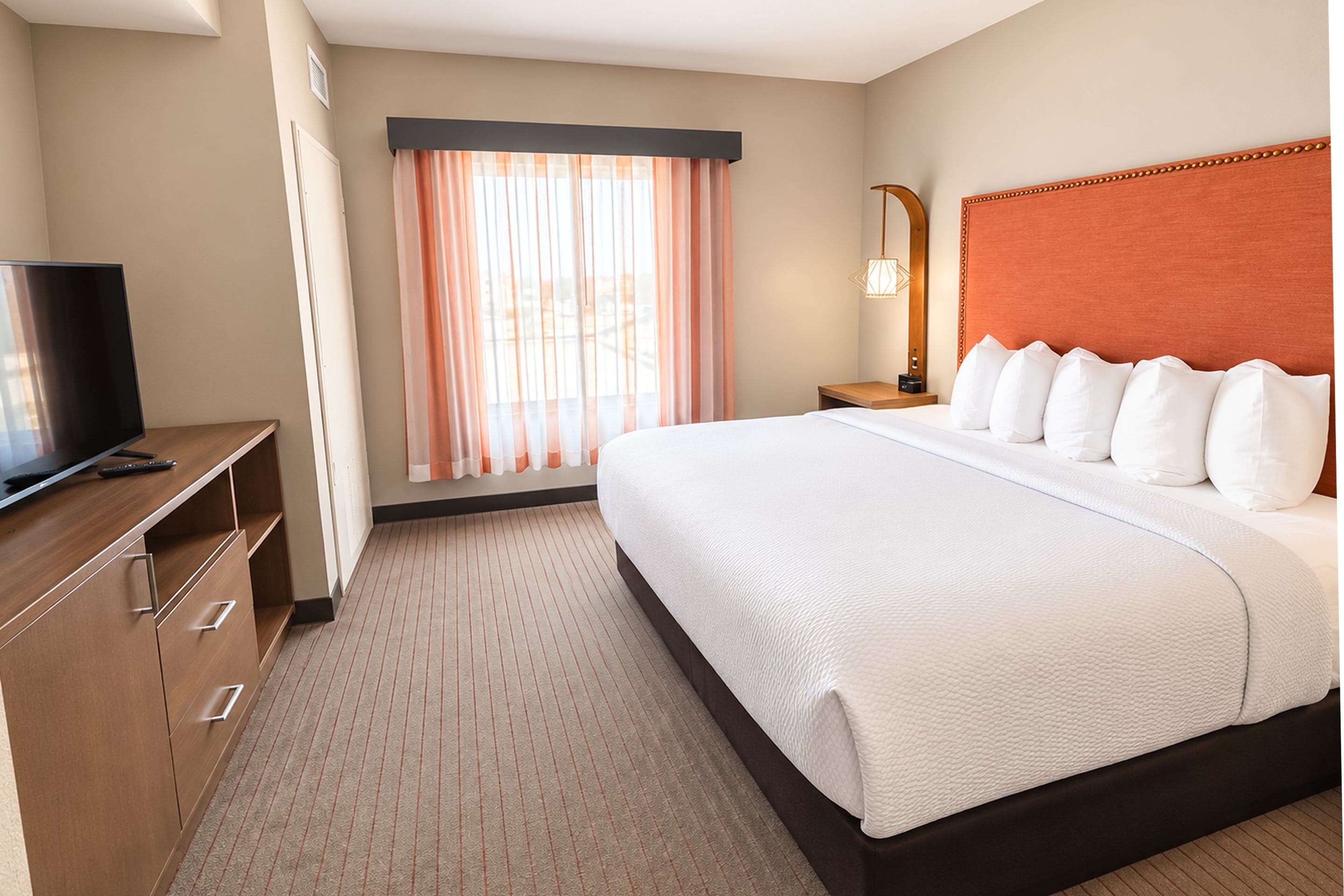 A hotel room with a bed, a TV, a desk, and a window with curtains.