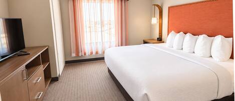 A hotel room with a bed, a TV, a desk, and a window with curtains.