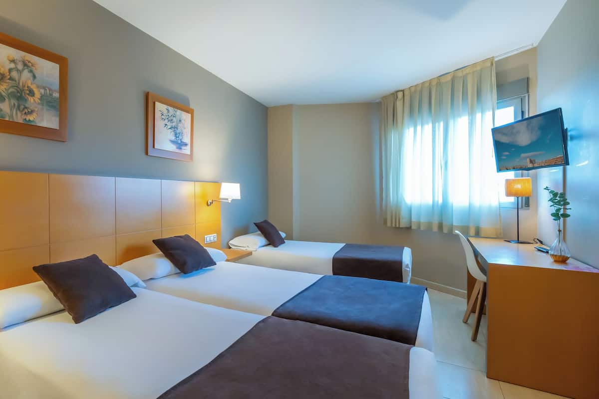 Habitación de hotel con dos camas, un escritorio, una silla, televisión y obras de arte en las paredes.