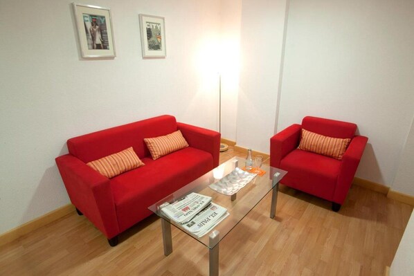 Ein Zimmer mit zwei roten Sofas, einem Glastisch und zwei gerahmten Bildern an der Wand.