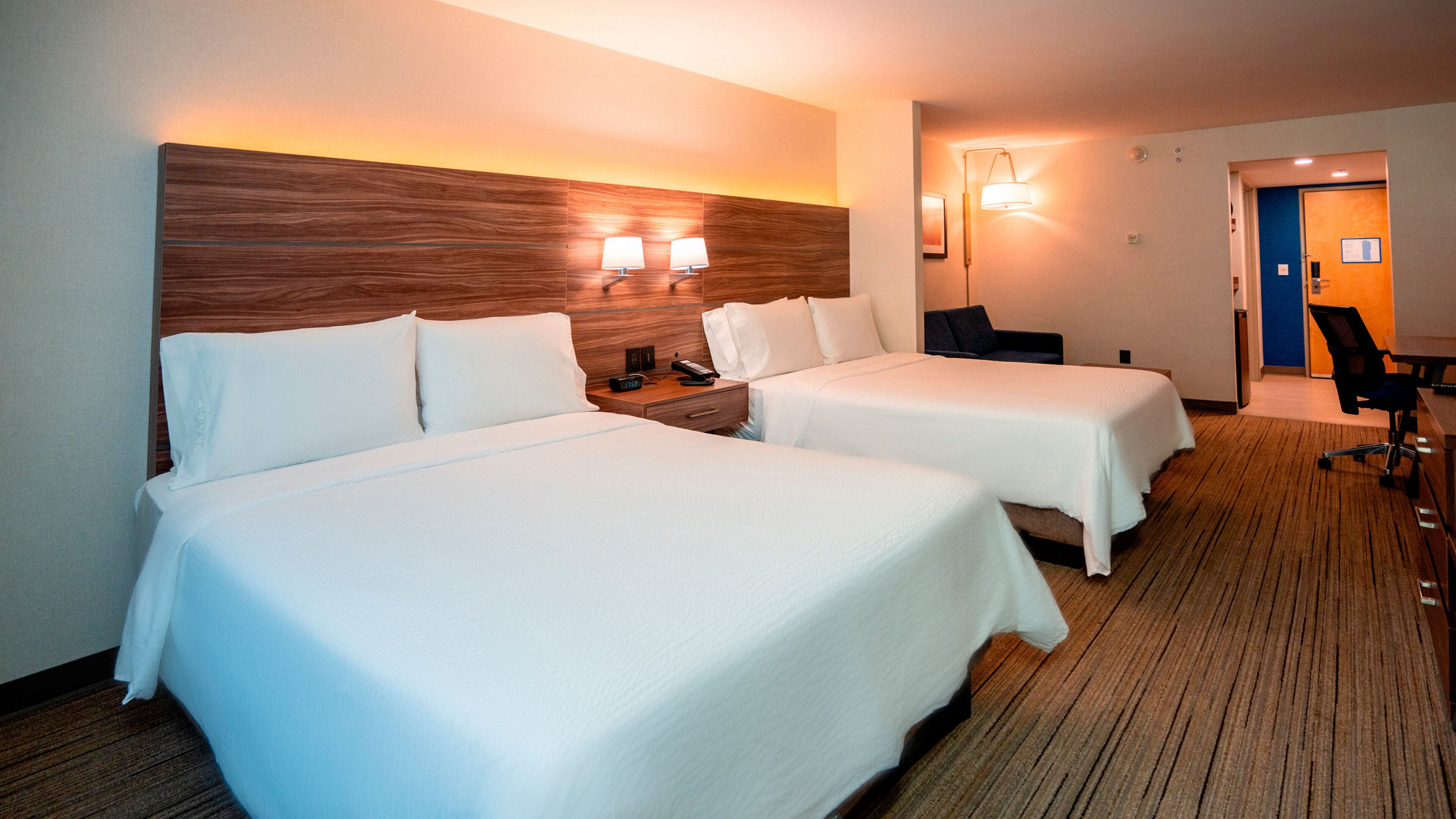 Habitación de hotel con dos camas, cabecero de madera, lámparas de noche, un escritorio y una silla.