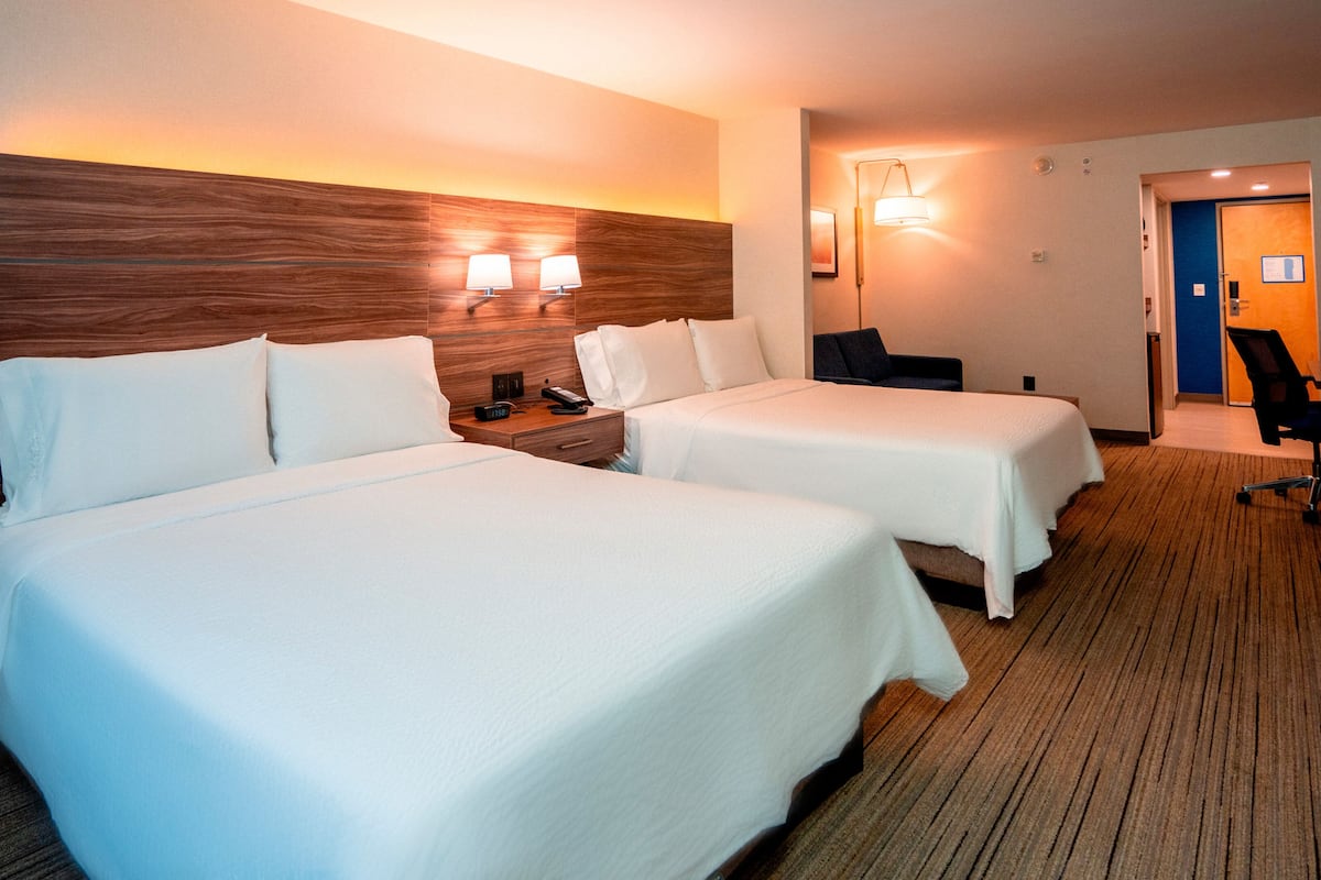 Habitación de hotel con dos camas, cabecero de madera, lámparas de noche, un escritorio y una silla.