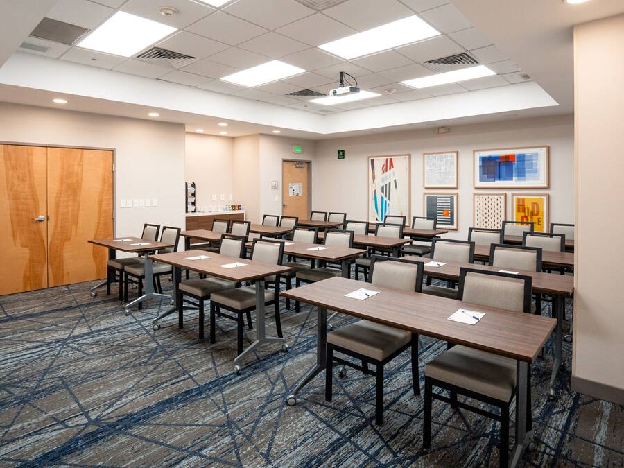 A conference room with multiple tables and chairs, a wooden door, and a carpeted floor.