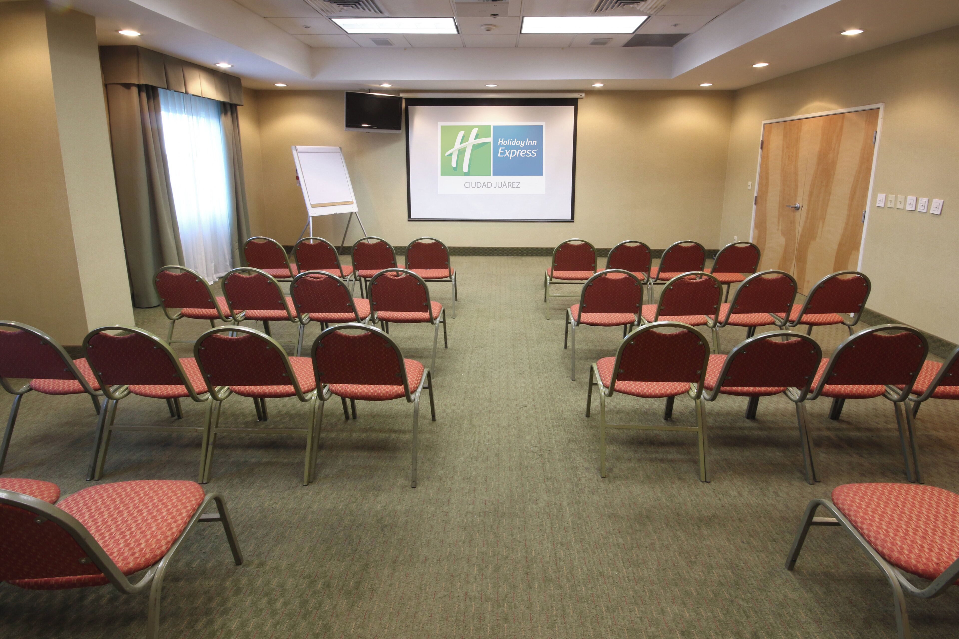 A conference room with rows of red chairs, a whiteboard, and a projector screen displaying a hotel name.