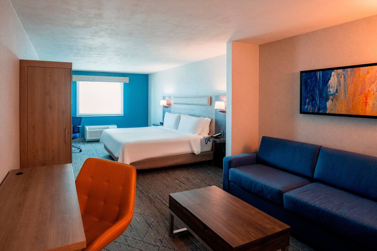 A hotel room with a bed, a sofa, a desk, and a chair.