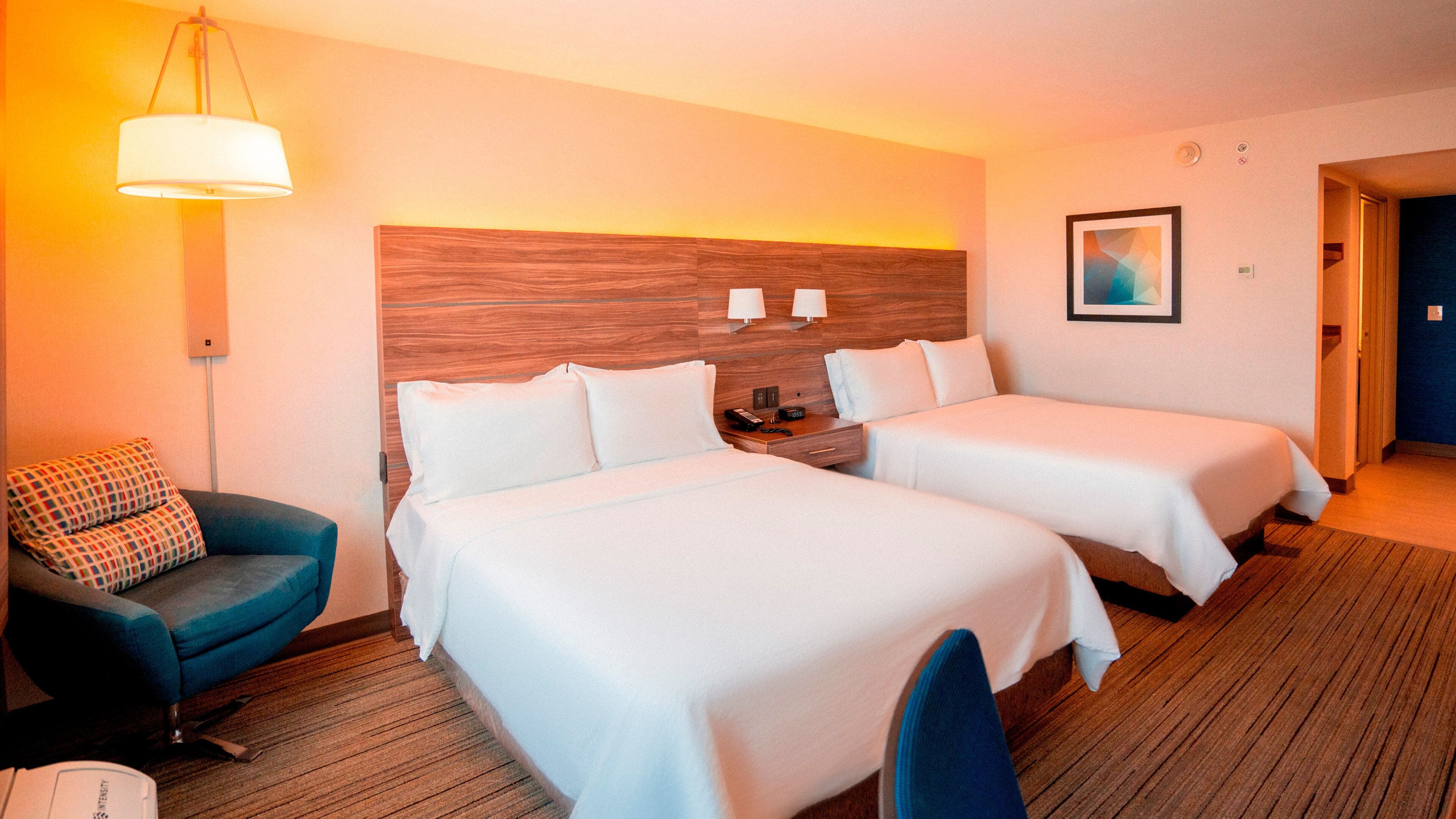 Habitación de hotel con dos camas, un escritorio, una silla, una lámpara y un cuadro en la pared.