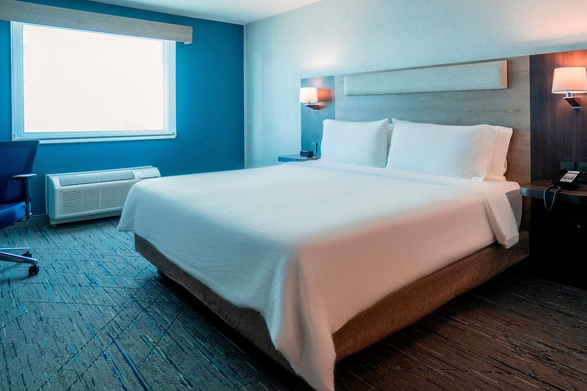 Habitación de hotel con una cama, un escritorio, una silla, una ventana y un teléfono instalado en la pared.