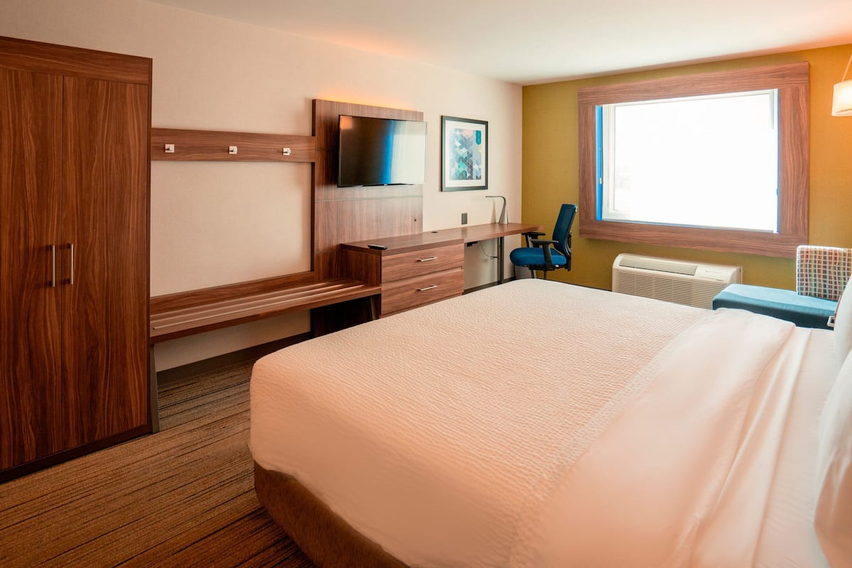 Una habitación de hotel con una cama grande, un escritorio con una silla, un televisor y una ventana con vistas.