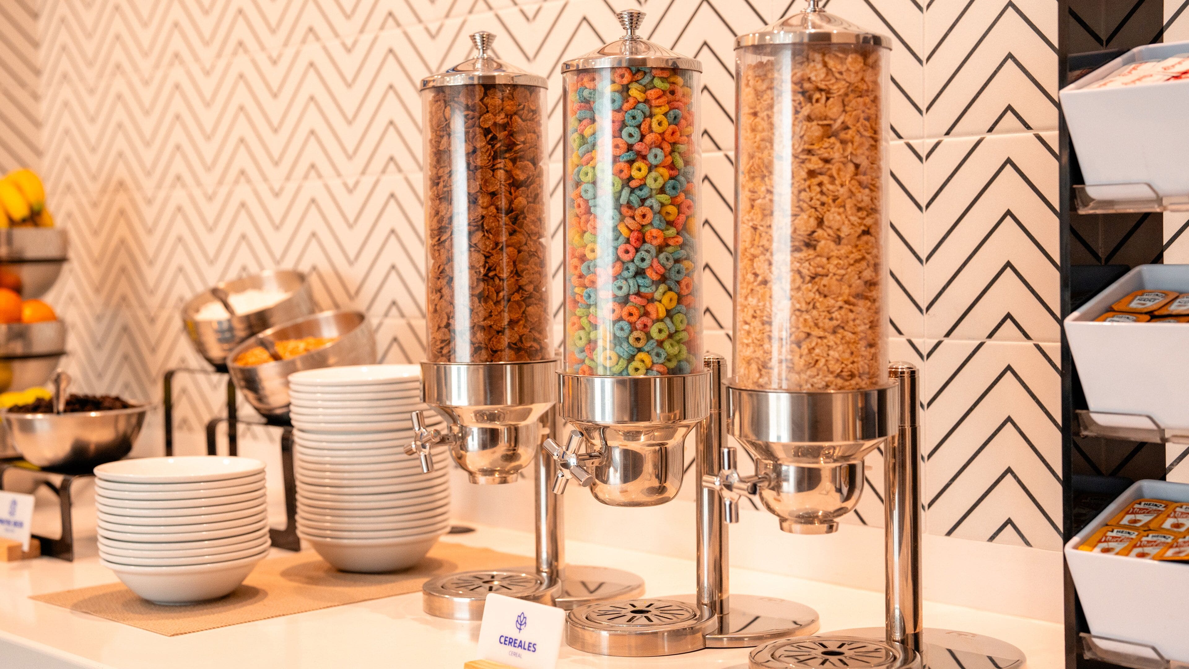 A breakfast station with cereal dispensers and stacked plates.