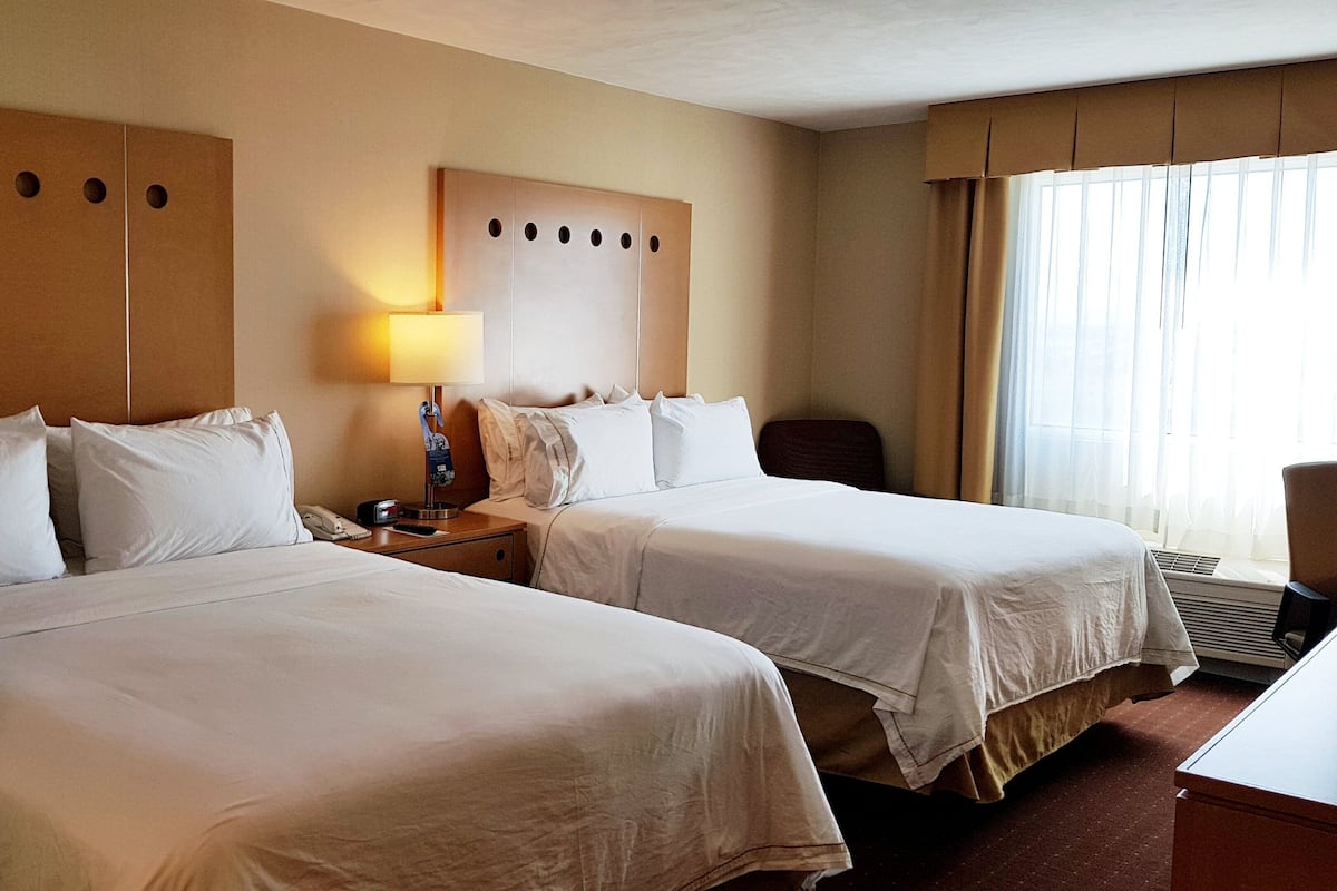 A hotel room with two beds, a nightstand, a lamp, and a window with curtains.