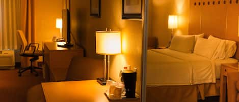 A hotel room with a bed, a desk with a lamp, a chair, and a coffee maker.